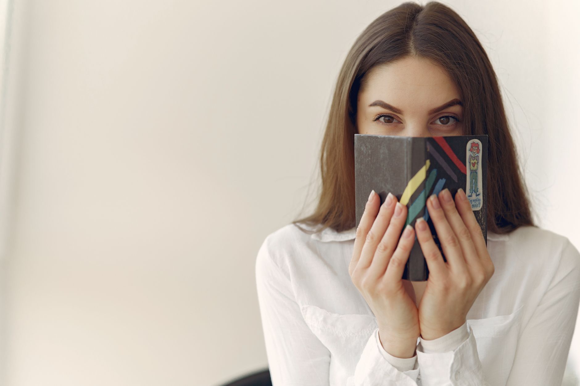 Persona joven tímida escondiéndose detrás de un libro, actitud característica del arquetipo dandere